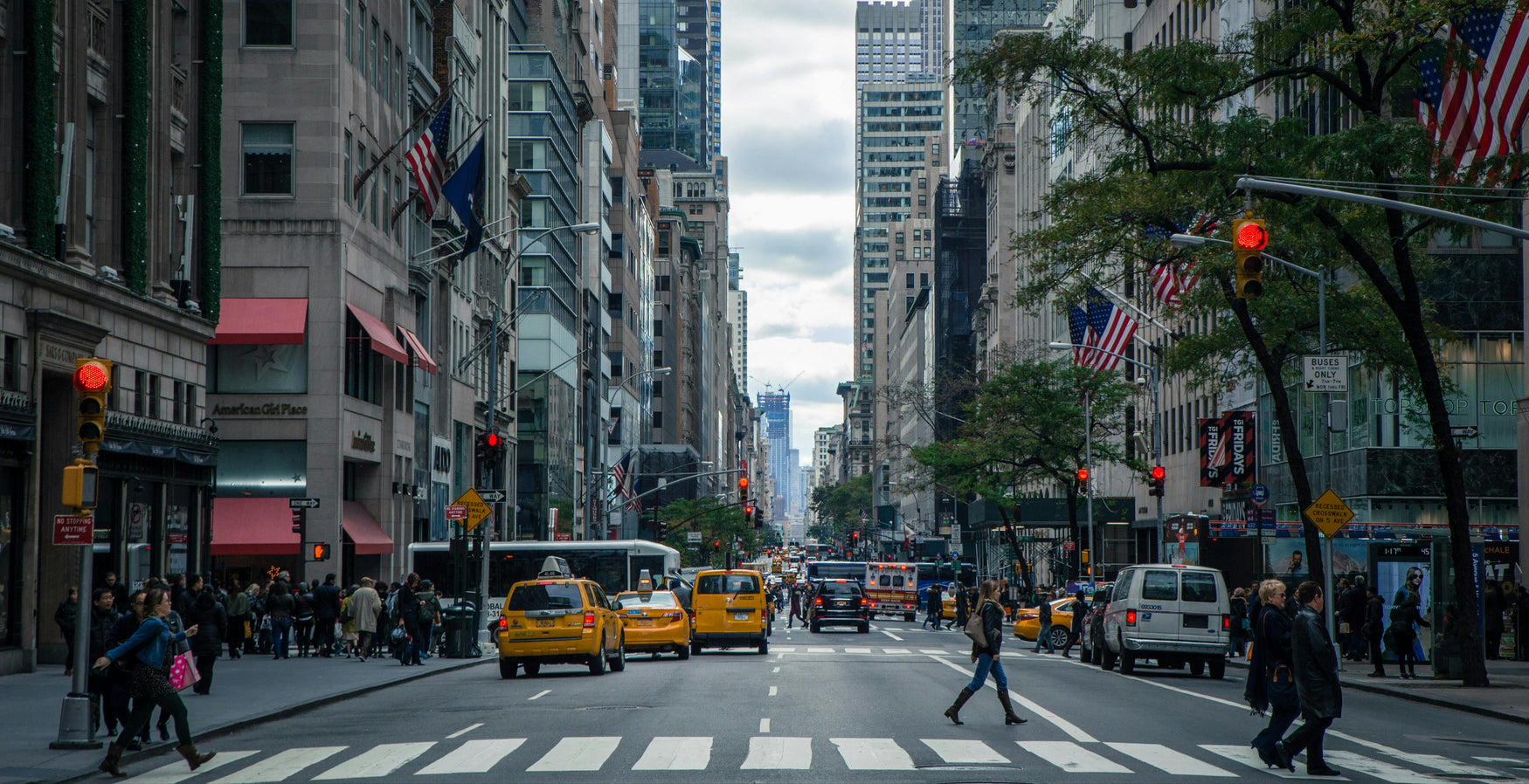 City street with tall buildings, taxis, and pedestrians on a cloudy day.